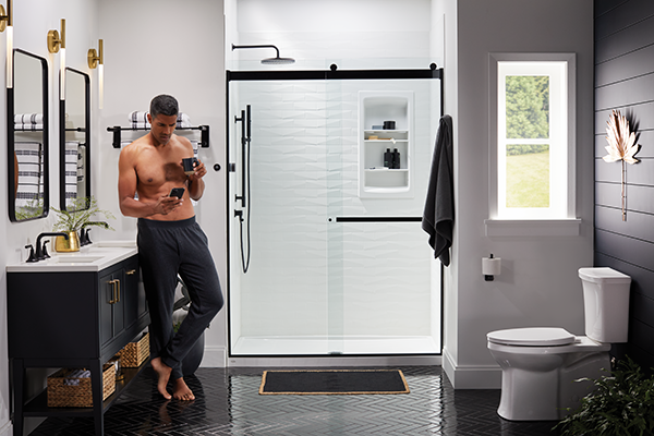 Modern bathroom with black vanity, glass sliding shower doors, built-in shower niches, and black-and-white design featuring a man standing by the sink.