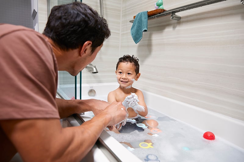 Father bathing young son in a modern bathtub during family bathroom remodel in Boulder, Colorado