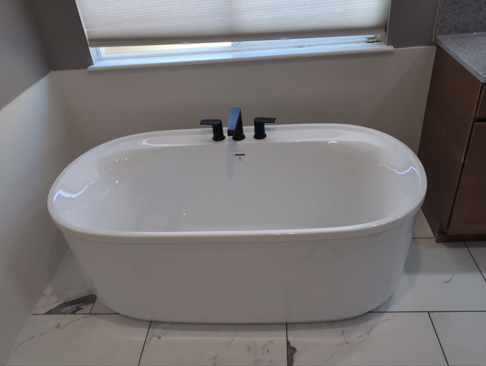 Oval freestanding tub with matte black fixtures and marble tile flooring in a Colorado Springs bathroom.