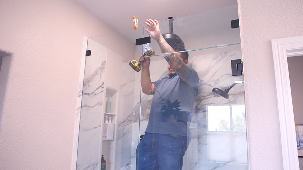 Contractor installing glass shower enclosure in Denver Metro bathroom remodel with marble-look walls