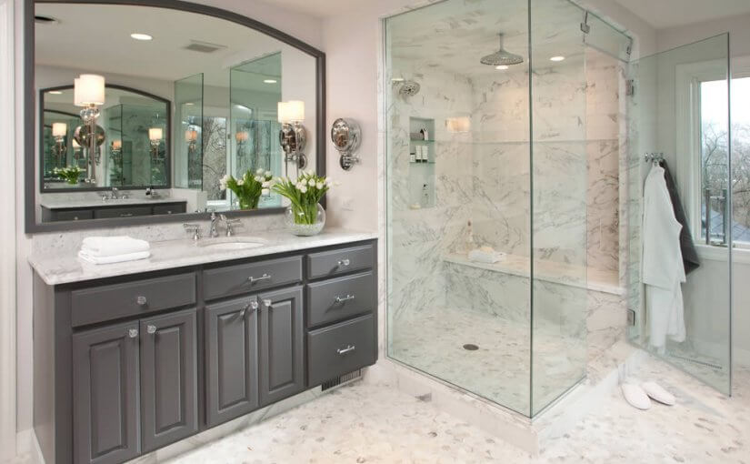 Luxury bathroom remodel with marble walk-in shower, glass enclosure, built-in bench, and gray vanity with dual sinks and large mirror.
