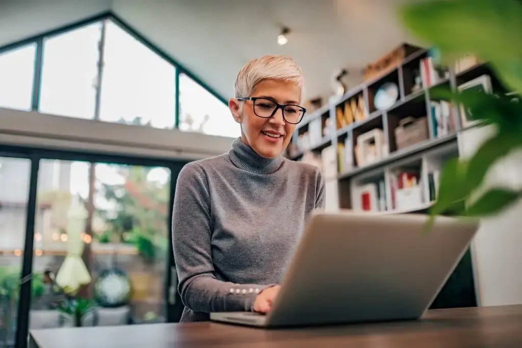 Smiling woman researching bathroom remodel ideas and reviews on a laptop at home.