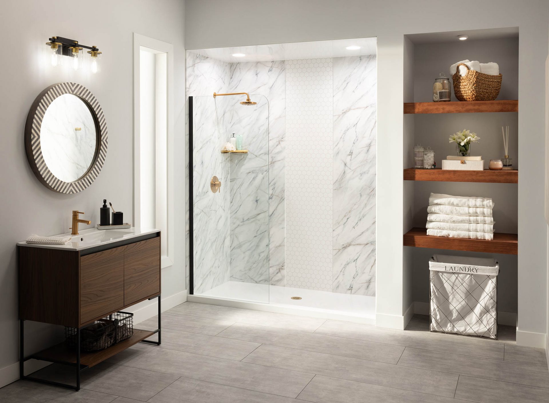 Modern bathroom remodel with marble-look walk-in shower, gold fixtures, floating wood vanity, round mirror, and built-in wood shelving with towels.