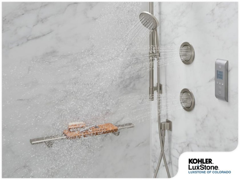 KOHLER LuxStone shower system with digital control panel, handheld showerhead, body sprays, and marble-look wall panels in a modern bathroom.